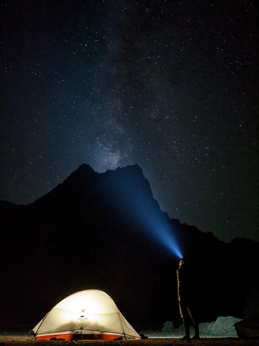 Night picture of a person next to tent that is looking with a headlight up to a starry sky with visible milky way