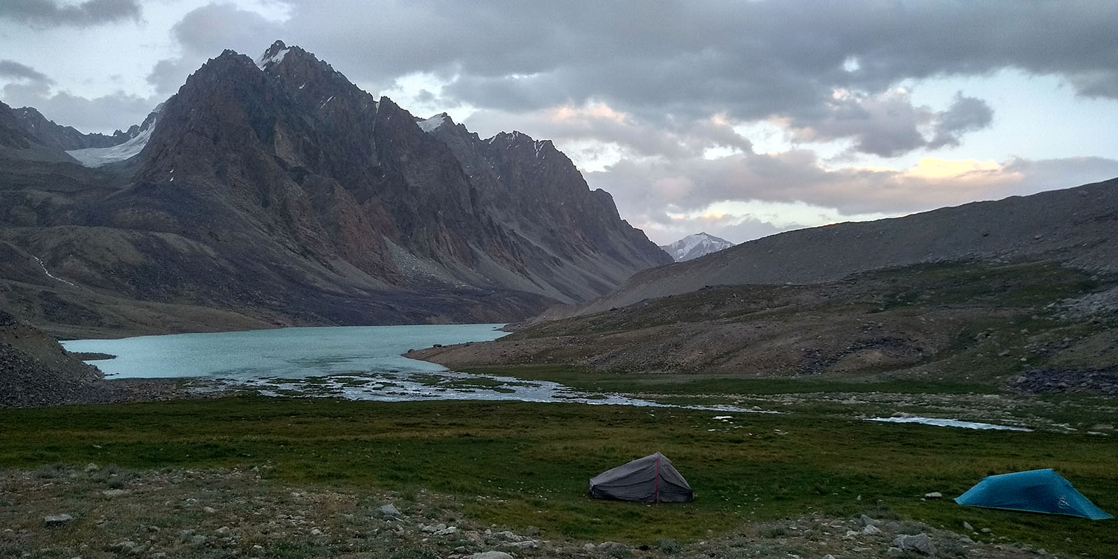 Two tents camped on a grass field next to Tsaxinkul