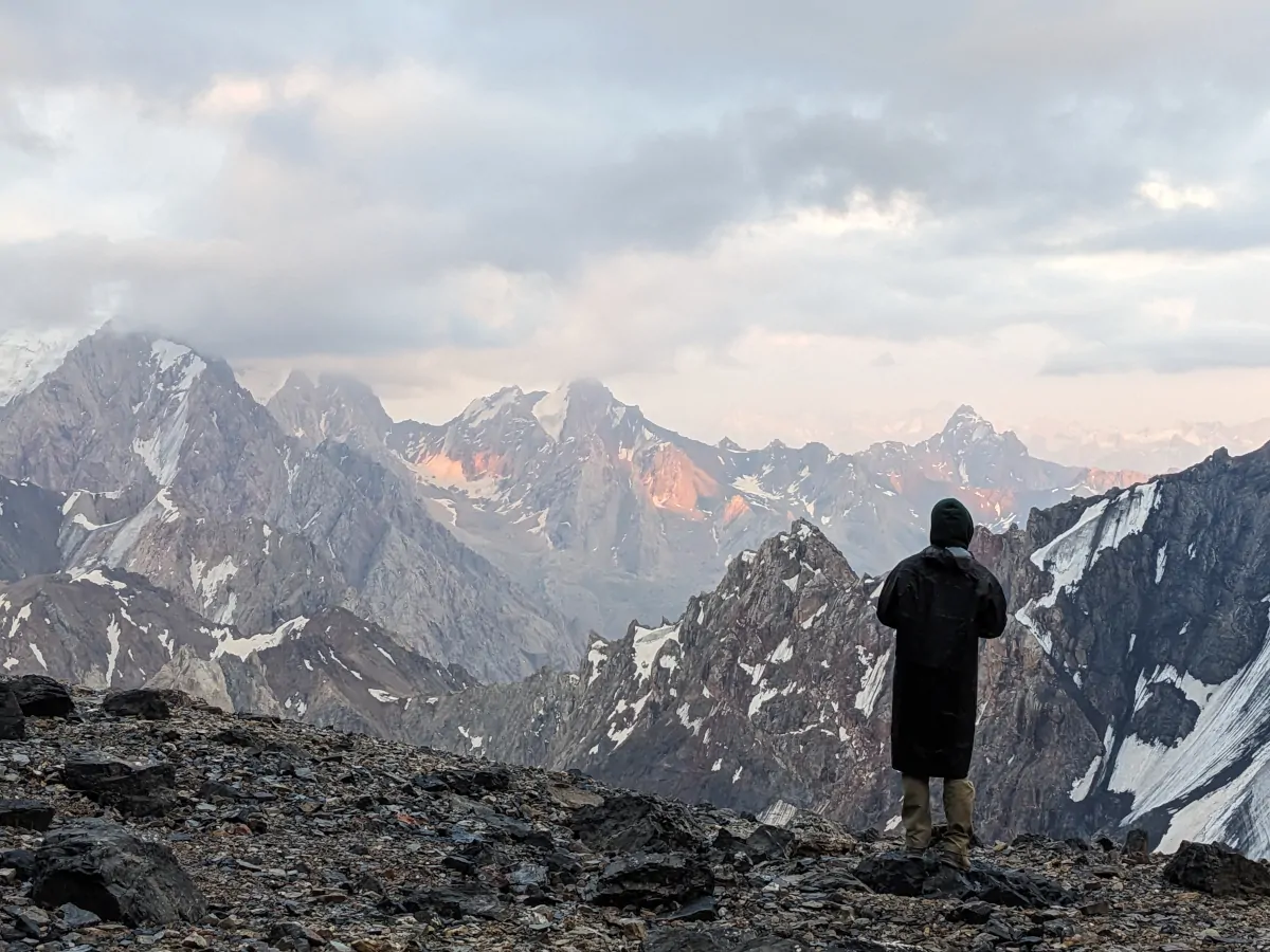 Man overlooking the Fann Mountains at sunset with redish highlights on the rocks in the distance