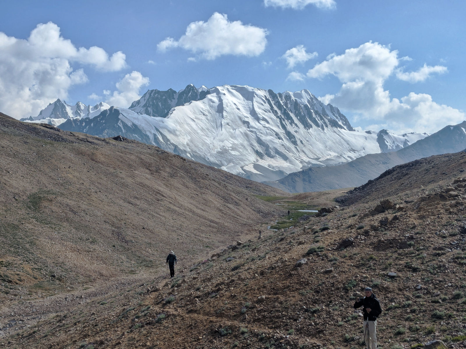 Hikers trekking across a rocky slope towards a huge mountain covered in snow