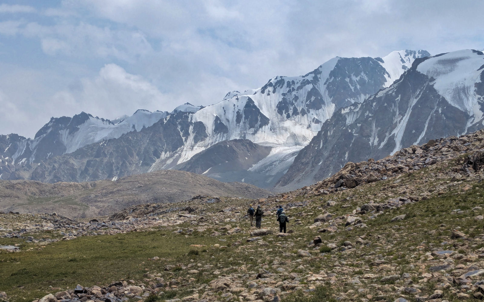 Four hikers with backpacks hiking away towards a mountain range covered by glaciers