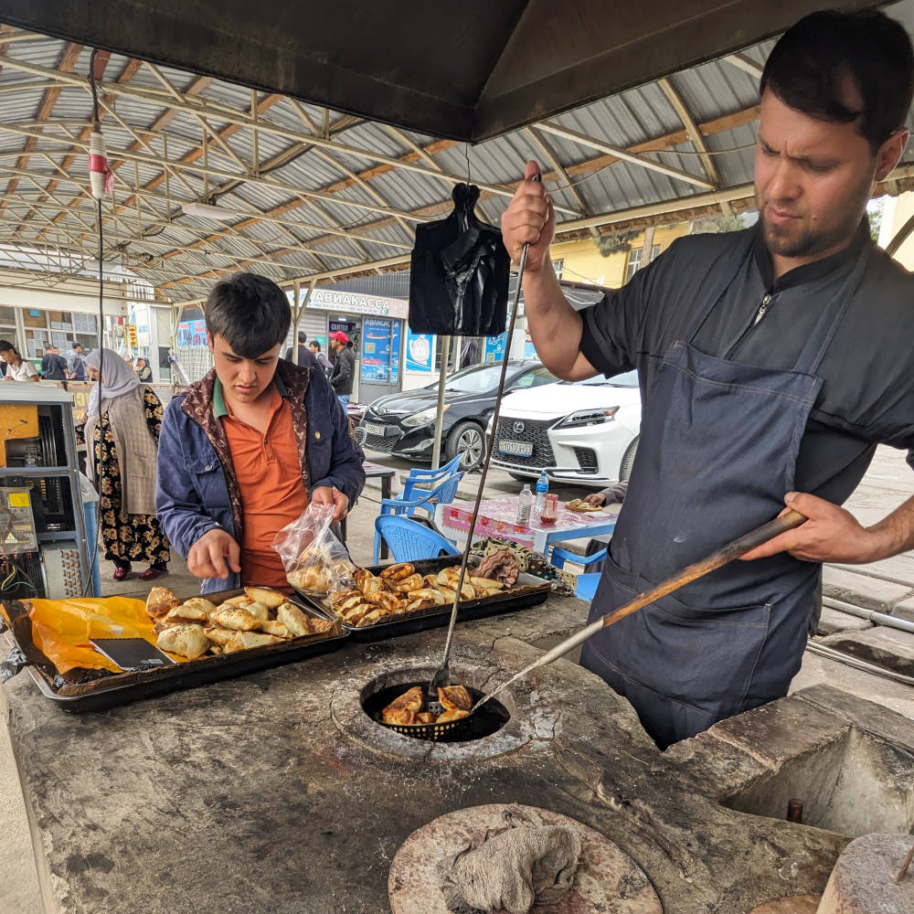 Man getting sambusa out from a tandi next to a vendor packing sambusa into bags