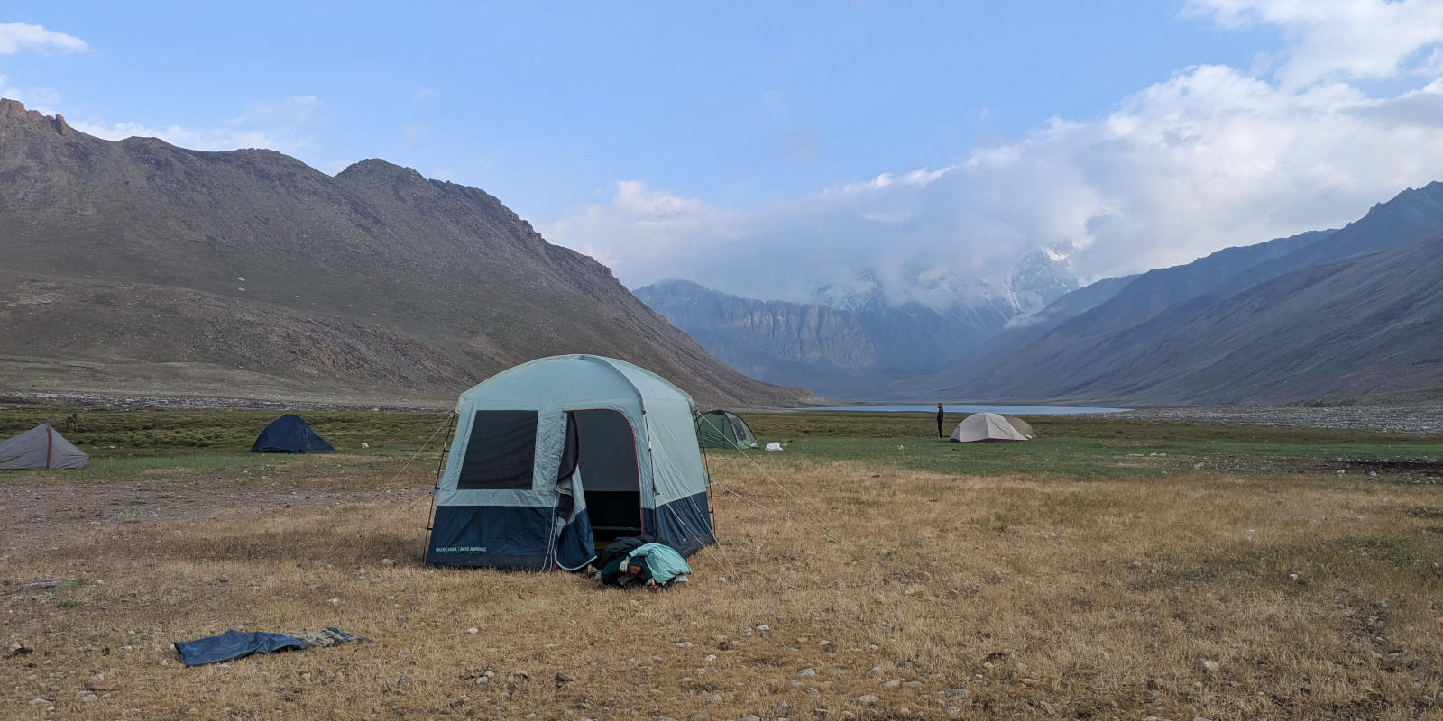 A group of tents surrounding a communal tent pitched on a vast grasland next to a lake in the Pamir Mountains
