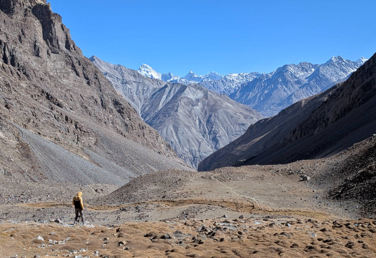 Person hiking down a slope towards snow-capped mountains of the Wakhan Corridor