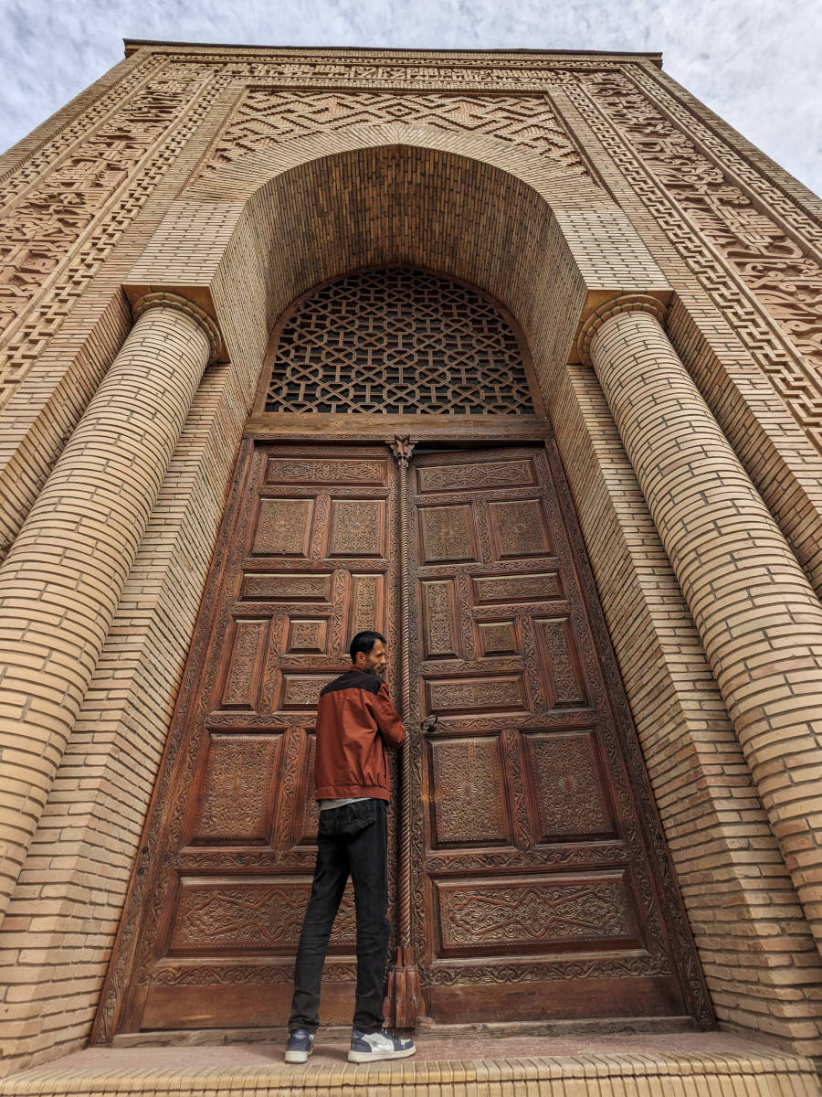 Man opening the main gate of the Hulbuk Fortress with intricate wood carvings