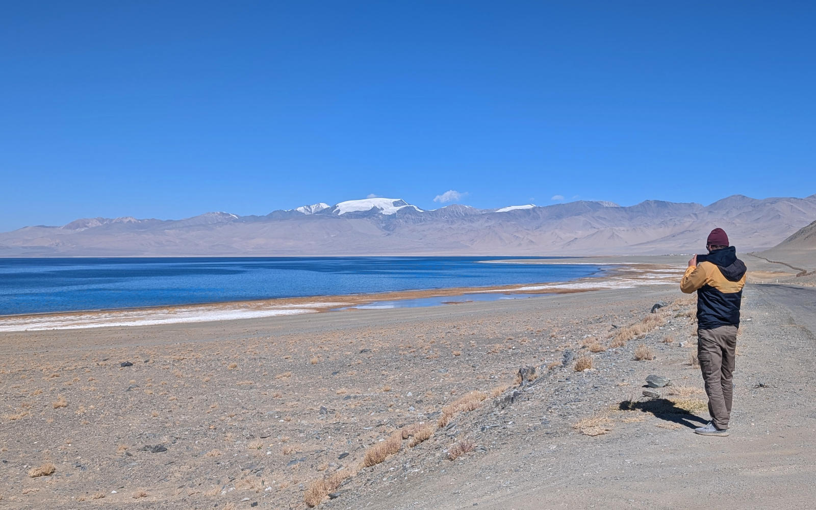 Person taking a photo of Karakul Lake with the mountain range defining the border with China in the background
