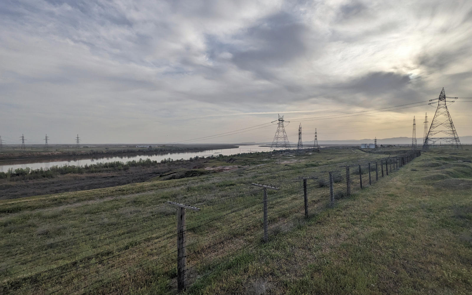 Fence along the Panj River separating Tajikistan from Afghanistan with electricity pylons and high-voltage cables across the river