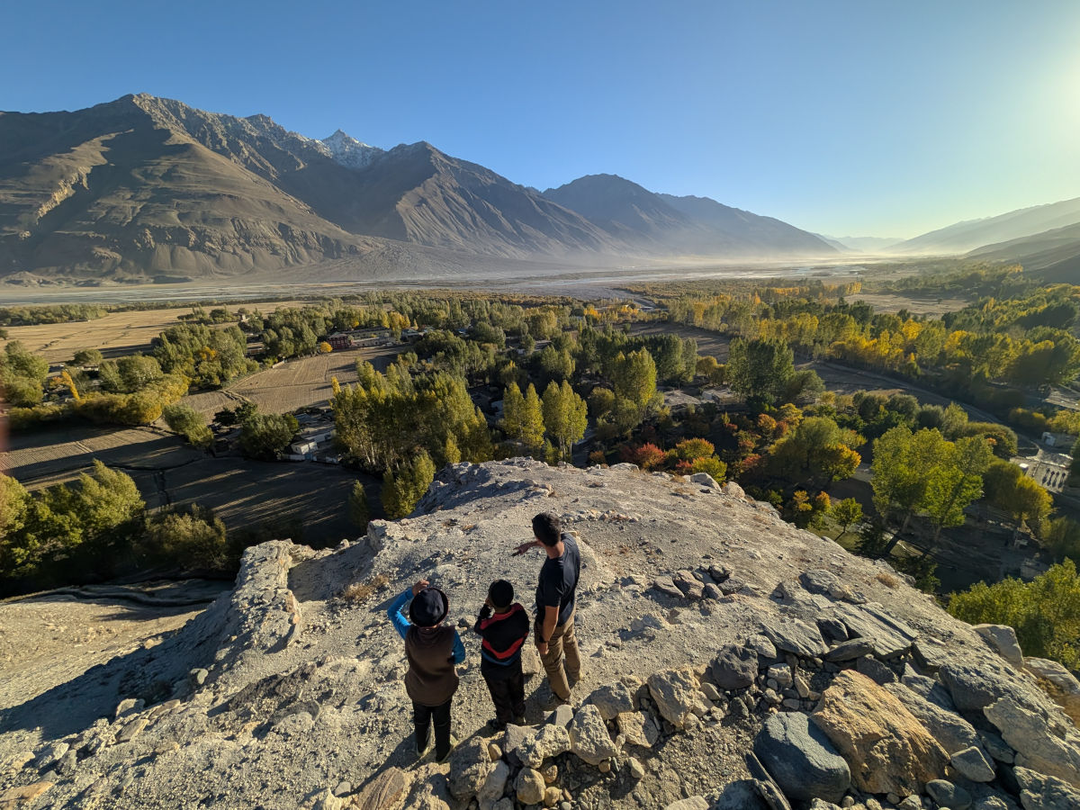 Three Pamiri people overlooking the Wakhan Valley close to sunset with many colorful trees